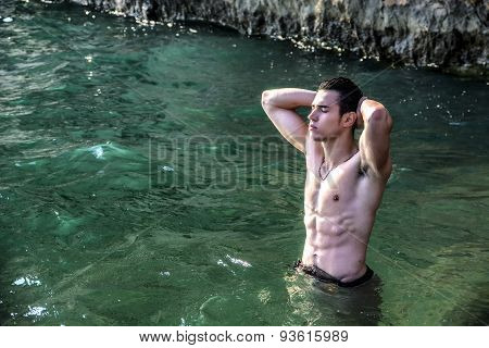 Young shirtless athletic man standing in water by ocean shore