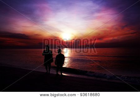 silhouette of a father and son walking on the beach at sunset.