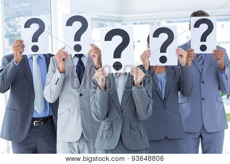 Business colleagues hiding their face with question mark sign at the office