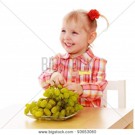 Blond little girl eating grapes sitting at the table