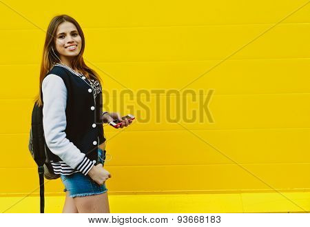 Happy young girl listening music  in headphones over yellowwall