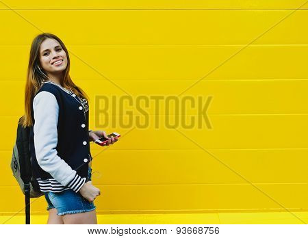 Happy young girl listening music  in headphones over yellowwall