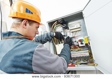 Young adult electrician builder engineer screwing equipment in fuse box
