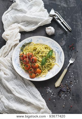 Pasta spaghetti with pesto sauce, basil, baked cherry-tomatoes on rustic wooden tabke dark table, to