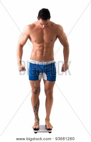 Muscular young man weighing himself on scale, making OK sign