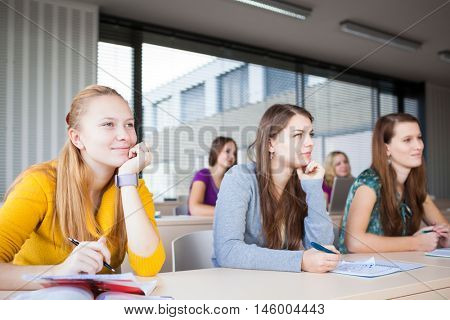 Students in classroom - young pretty female college student sitting in a classroom full of students during class (color toned image; shallow DOF)