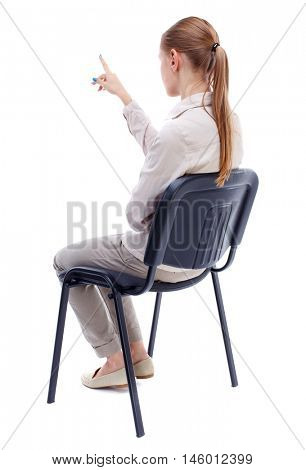 back view of young beautiful woman sitting on chair and pointing. Skinny girl in white denim suit sidit thoughtfully in his chair and points.