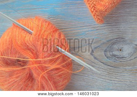 Knitting orange mohair wool ball and knitting needles on the old wooden rustic background. The beginning on knit cloth