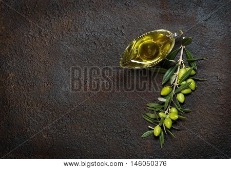Top view of branch with green olives and glass sauceboat of olive oil on a black grunge metal background.
