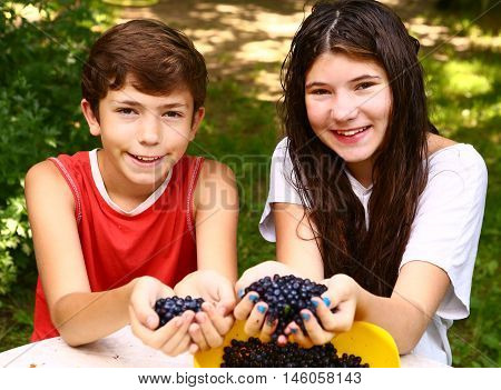 teenager siblings brother and sister with handful of bilberries close up smiling portrain on the green grass summer background