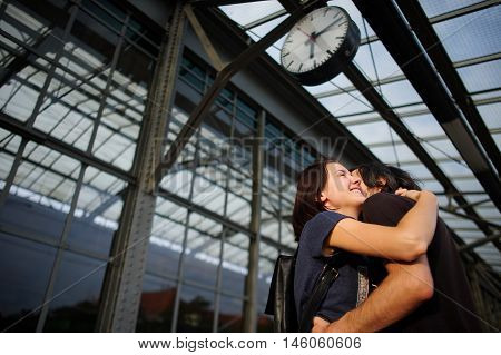 Loving couple met or parted on the platform under the clock. The young man put his arm around the girl. Girl smiling happily.
