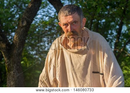 Portrait of tired bee-keeper wearing dirty linen shirt at work place