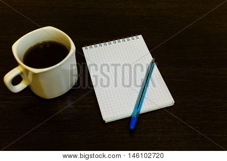 White notepad with a pen on a brown table with a cup of coffee