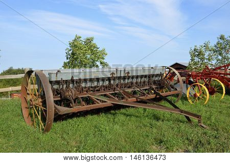 An old grain drill with a metal box to hold seed for planting small grain is parked in the grass.