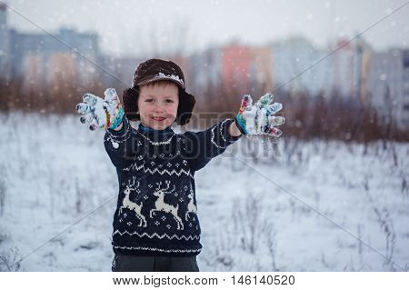 Winter portrait of little kid boy wearing a knitted sweater with deers outdoors during snowfall. Active outdoors leisure with children in winter on cold snowy days.