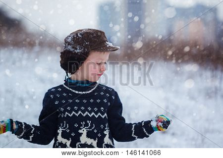 Winter portrait of little kid boy wearing a knitted sweater with deers outdoors during snowfall. Active outdoors leisure with children in winter on cold snowy days.
