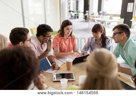 education, high school, people and technology concept - group of international students sitting at table with tablet pc computers, books and notebooks at university