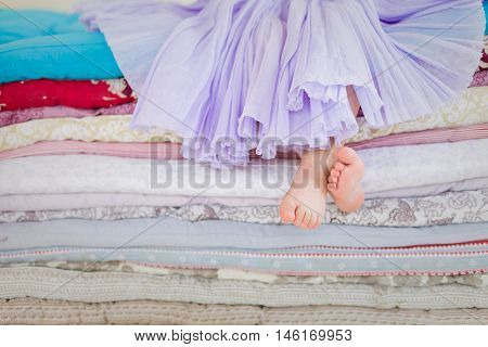 The fairy tale the princess on a pea. Little girl in lilac tatu skirt sitting on the high bed. Bare foot if the girl. Legs of a little girl sitting on a pile of colorful mattresses.