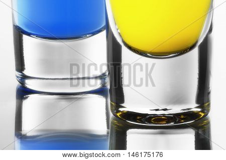 Blue and yellow cocktails in clean shot glasses. Downside of shot glasses with own reflection.