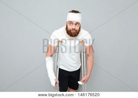 Confused bearded young man standing with crutches over white background