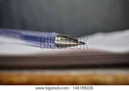 Detail of a sharp tip of the blue ball pen on the white lined notepad as a symbol of business office stationary