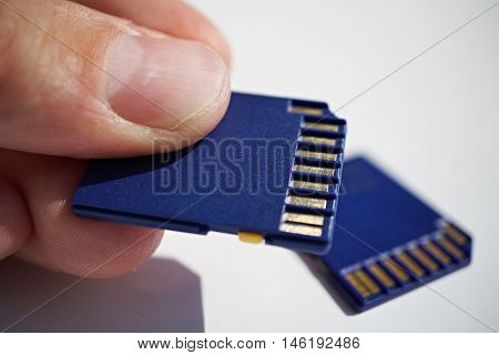 Male hand holding a memory card (SD card - Secure Digital card) used in video cameras and  computers in blue color as a symbol of technology used for home and professional entertainment