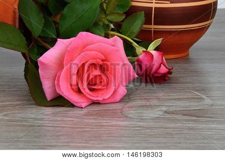 Capsize flower vase with roses. Water leaked out of a vase. The vase is a wooden base.