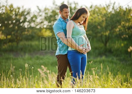 Happy Pregnant Couple At Garden On Magestic Sunset
