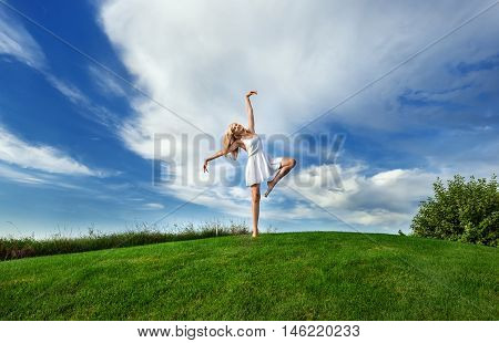 Caucasian white woman dancing in white short dress on a background of green grass and blue sky with clouds