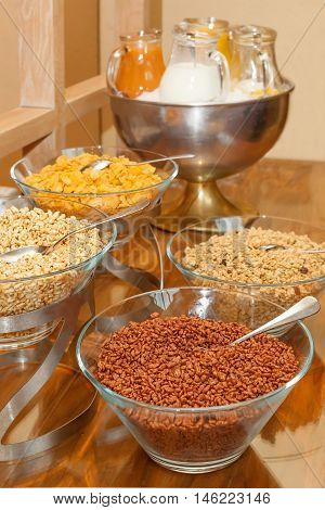 Buffet variety of cereals for breakfast-cereals in glass bowls, milk and juice in glass pitchers, vertical