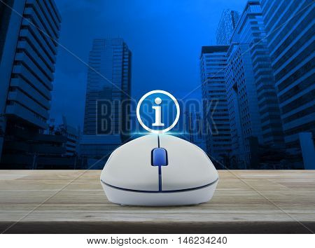 Wireless computer mouse with information sign icon on wooden table over city tower background