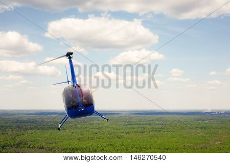 The aircraft - the small blue helicopter flight against the background of the cloudy sky.