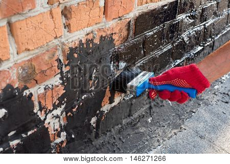 Roofer covered brick wall bitumen primer for improving adhesion during surfacing contiguity with rolled waterproofing during the installation of flat roof.