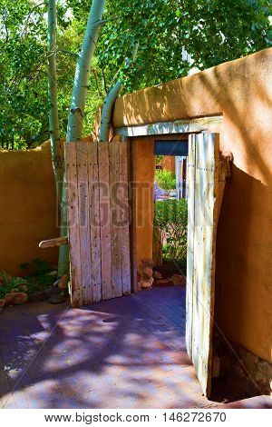 Rustic adobe style wooden door with Spanish Colonial architectural design which opens to a courtyard garden taken in Santa Fe, NM