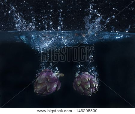 two artichokes splashing in the water with bubbles