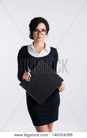 Young Caucasian woman wearing a dark blue dresst and and a white shirt, holding a ring binder folder and pen. Isolated on light background