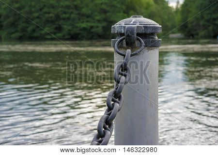 The bar for the protection of the pier with a chain on a background of the river and trees
