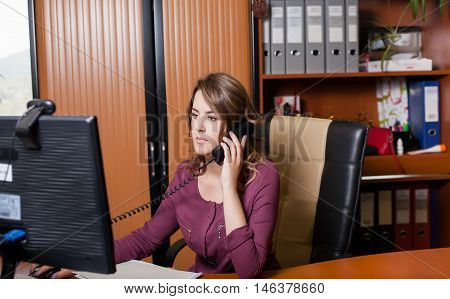 Young office woman worker talking on phone. Sitting on a chair at the table