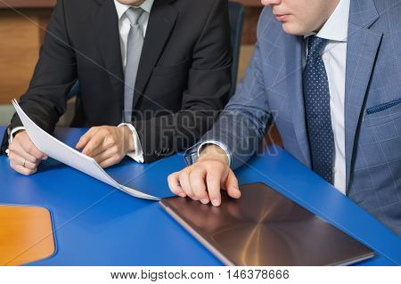 Business meeting People sitting for a glass table with business plan on high floor in the office. Man in suit shows a business graph of his business partner.