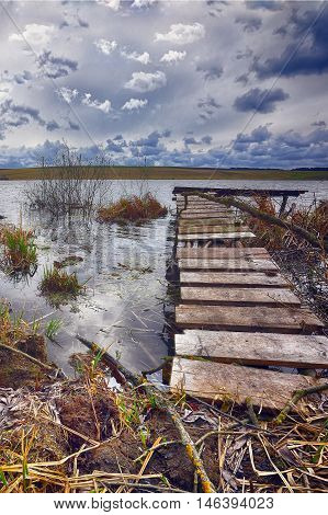 Old wooden pier with dry reed. Cloudy weather. Dramatic sky