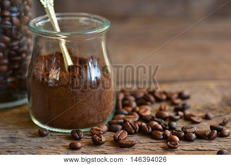 Ground coffee in a glass jar with coffee beans on a wooden background