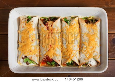 Mexican burittos in a baking dish. Shot from above over wooden background