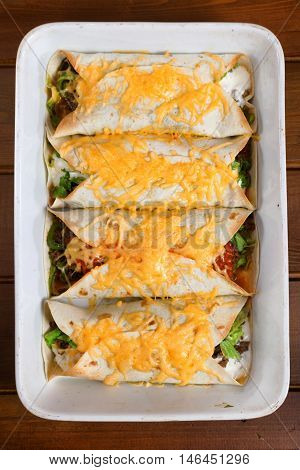 Mexican burittos in a baking dish. Shot from above over wooden background. Vertical shot