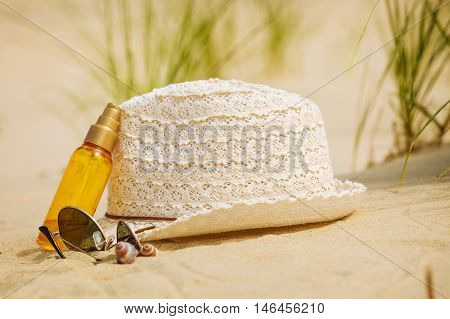 Summer vacations concept. Beach accessories. Straw hat sunglasses and sun oil on sand.