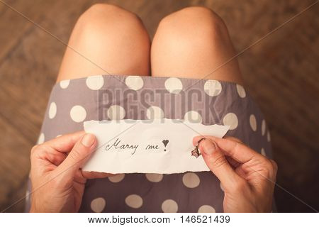 Hand holding a note of paper with the message marry me on it and a ring on her finger