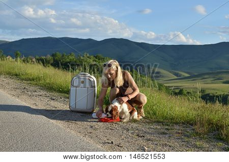 Woman taking care of her dog giving her water from a dog's water container on a mountain road on sunny day