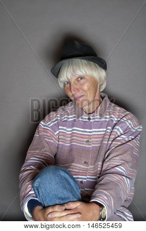 Female with gray hair and wearing men hat posing in studio with a sneering look on her face.