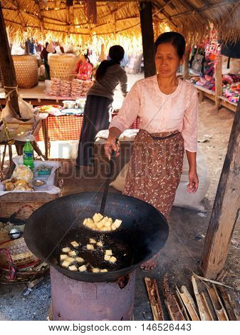Heho Myanmar - March 03 2011 - Old Burmese woman cooking street food at five-day market while sitting on the ground