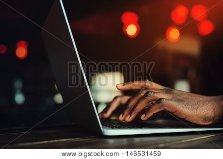 Black man's hands typing on laptop keyboard. Person working with laptop. Beautiful lights as background. Toned.