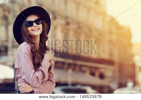 Outdoor portrait of a young beautiful fashionable happy lady posing on a street of the old city. Model wearing stylish clothes. Girl looking up. Female fashion. City lifestyle. Copy space for text.